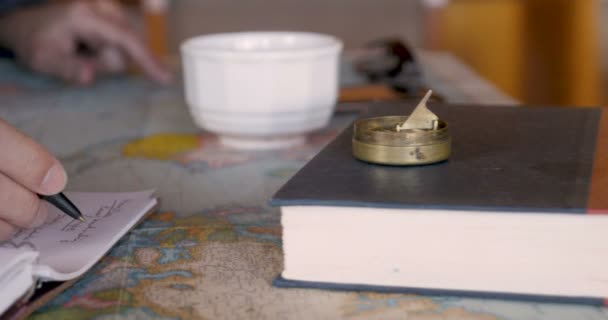 Ένα χέρι που γράφει σε ένα σημειωματάριο πάνω σε έναν παγκόσμιο χάρτη σε κοντινό πλάνο — Αρχείο Βίντεο