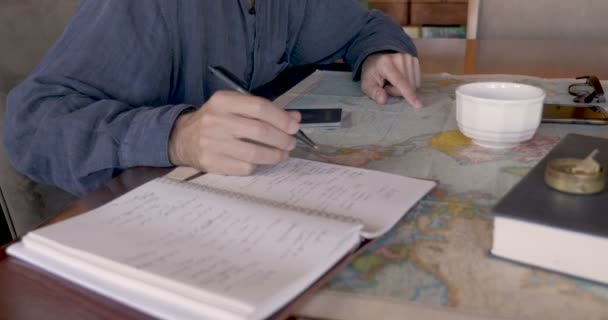 Side view of man researching places to travel to using map and notebook — Stock Video
