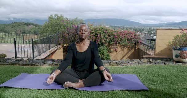 Zdravé africké americké vyšší sezení zkříženýma nohama meditující venku — Stock video