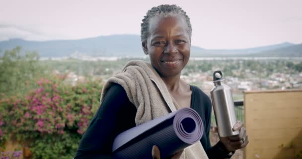 Mosolygó idős afroamerikai vezető tartó női jóga mat és a vizes palack — Stock videók