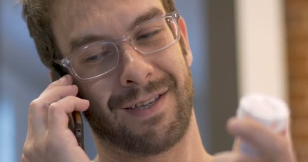 Bonito homem com barba segurando garrafa de remédio e falando no telefone inteligente CU — Vídeo de Stock