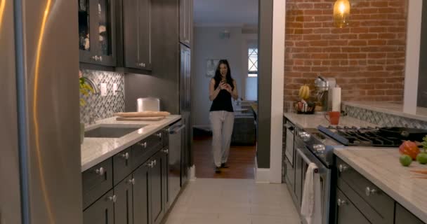 Frau betritt ihre Kombüsenküche tanzend mit ihrem Smartphone — Stockvideo