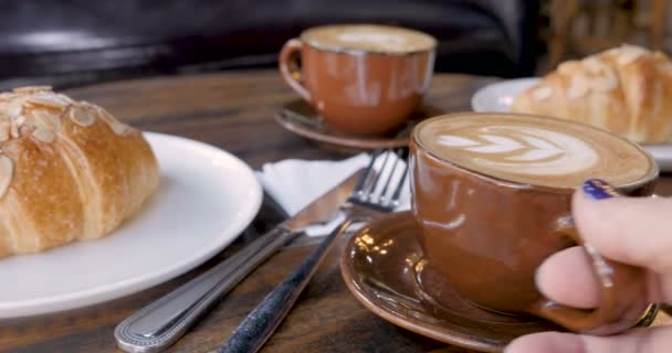 Vrouw hand neemt een kopje koffie en zet het terug naast de croissants — Stockvideo