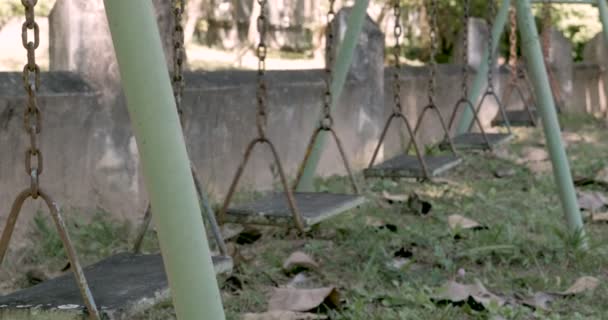 Um único balanço movendo-se para trás e para a frente em um playground abandonado — Vídeo de Stock