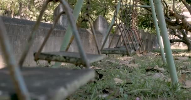 Unghiul scăzut al unui singur leagăn care se mișcă înainte și înapoi în terenul de joacă abandonat — Videoclip de stoc