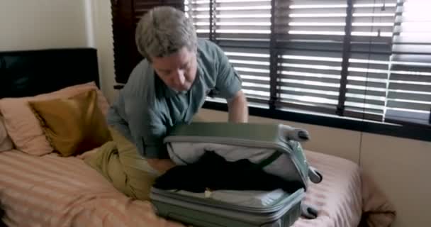 Hombre tratando de cerrar su bolsa de viaje lo deja caer en el suelo mientras empaca — Vídeos de Stock