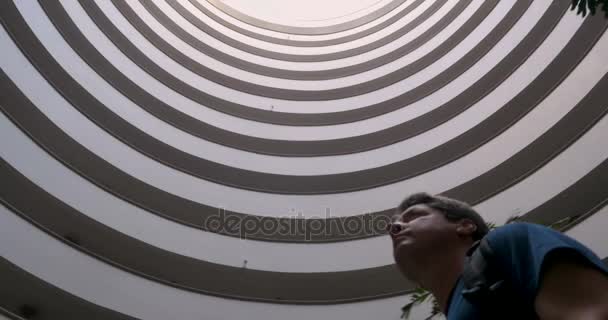 Traveling man with backpack looking up at the sky through round building — Stock Video