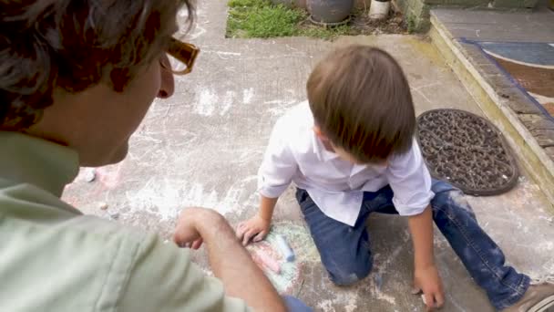 Чарівний молодий хлопчик з крейдою на всіх штанях малює з батьком — стокове відео