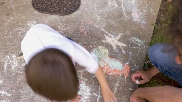 Au-dessus d'un jeune garçon dessinant à la craie en utilisant les deux mains avec son père — Video