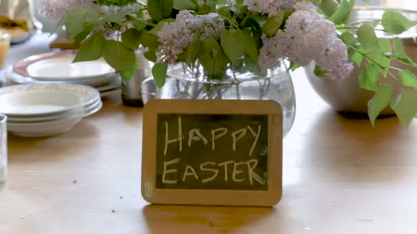 Glad påsk skrivit på en liten krita ombord mot en vas med vackra blommor — Stockvideo