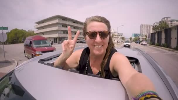Joyeux blond femme se selfie tout en se tenant à travers un toit ouvrant dans une voiture — Video