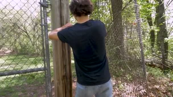 Man breekt door een ketting link hek en lopen in het bos — Stockvideo