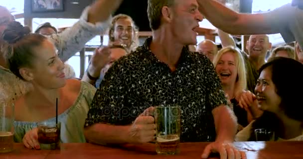 Велика група людей підбадьорює чоловіка, який сидить у барі — стокове відео