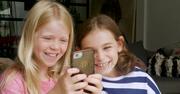 İki genç kız gülüyor ve birlikte bir cep telefonu kullanırken gülümseyen arkadaşlar — Stok video