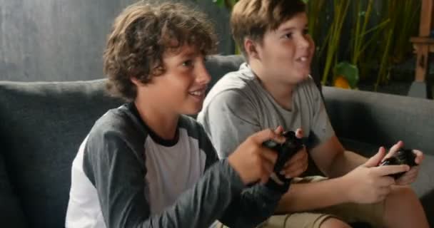 Casal de jovens meninos pré-adolescentes jogando videogames em um sofá — Vídeo de Stock