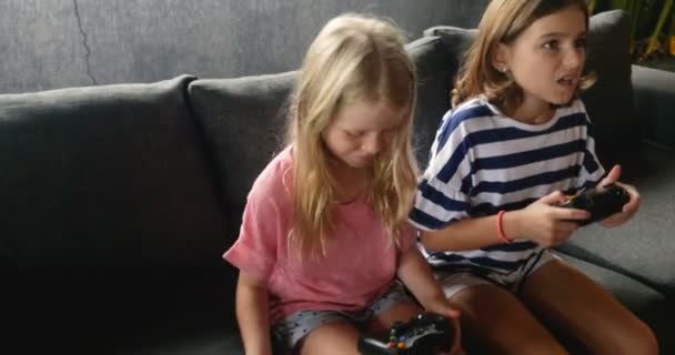 Two young cute girls playing video games together on a sofa