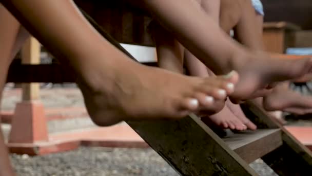 Een groep jonge barefoot kinderen hun benen heen en weer slingeren — Stockvideo