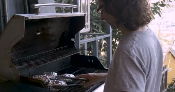 Homem usando pinças de metal para virar batatas envoltas em folha de alumínio em um churrasco — Vídeo de Stock