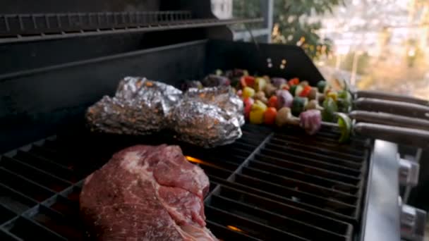 Grand steak de bœuf grillé sur un barbecue avec un homme tournant des kebabs de légumes — Video