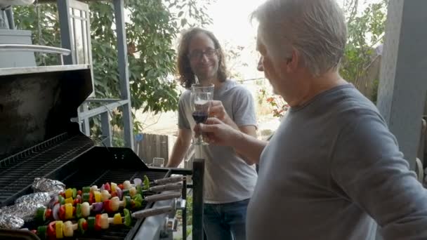 Mayor padre e hijo asar kebabs de verduras a la parrilla en una barbacoa beber — Vídeos de Stock