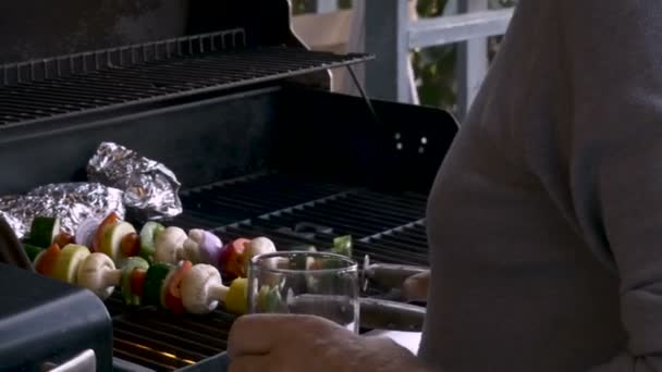 Senior elderly man in his 70s placing healthy veggie shish kebabs on a hot bbq — Stock Video