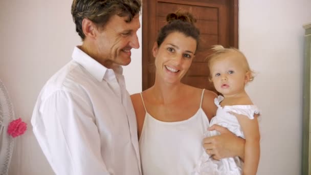 Ευτυχισμένη οικογένεια χαμογελαστός, φορώντας λευκό με ένα χαριτωμένο μωρό, κορίτσι στέκεται — Αρχείο Βίντεο