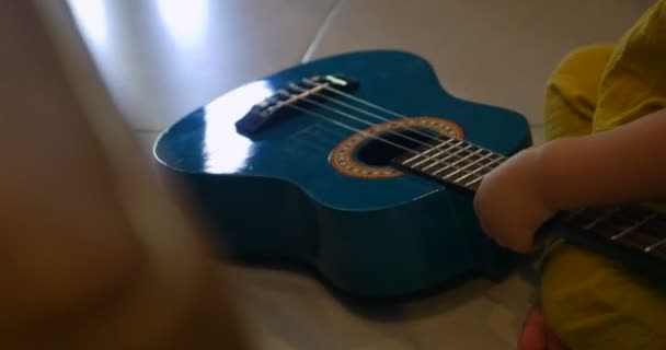 Мила дитина грає з маленькою іграшковою гітарою, сидячи на підлозі — стокове відео