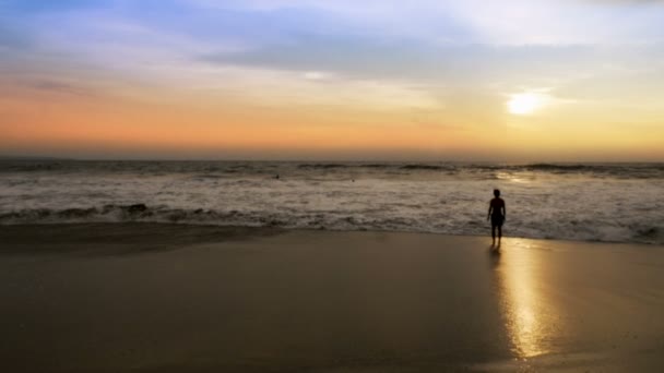Uomo guardando il tramonto come l'onda dell'oceano ottiene i piedi e le gambe bagnate — Video Stock