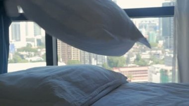 Ağır çekimde modern bir şehir manzaralı bir yatakta yastık hele kadın