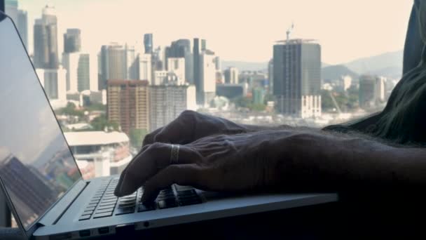 Die Hand eines Mannes tippt auf einer Laptop-Tastatur mit Blick auf eine moderne Stadt — Stockvideo