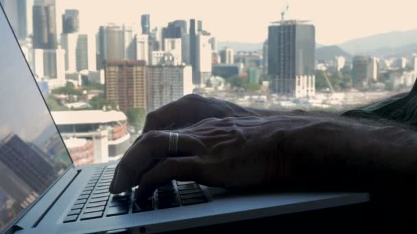 Χέρια πληκτρολόγησης σε ένα φορητό υπολογιστή με θέα μια μοντέρνα και πολυσύχναστη πόλη — Αρχείο Βίντεο