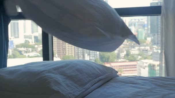 Femeie pufoasă perne pe un pat cu vedere la un oraș modern în mișcare lentă — Videoclip de stoc