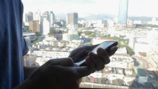 Close up de um homem segurando um telefone inteligente com vista para uma cidade com arranha-céus — Vídeo de Stock