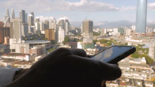 Refleksje drapaczy chmur są widoczne w telefon mężczyzny, podczas gdy on jest wpisanie — Wideo stockowe