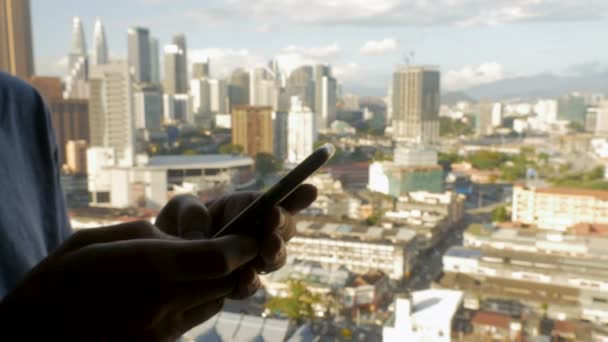 Volar sobre un hombre escribiendo en su teléfono celular con vistas a una ciudad moderna — Vídeos de Stock