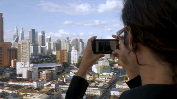 Туристичні людина, використовуючи свій мобільний телефон прийняти фотографії великого міста подання — стокове відео