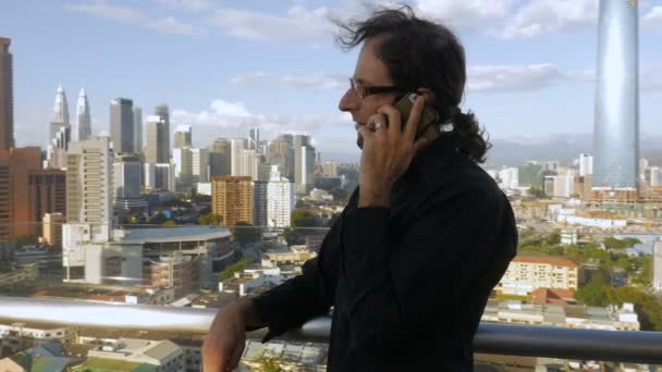 Framgångsrik man pratar på en smart telefon på ett hustak som tittar över en stad — Stockvideo