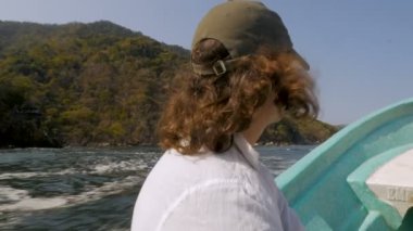 Hareketli bir tekne bir dağlık deniz sahil hattı yakınlarında oturan uzun saçlı adam