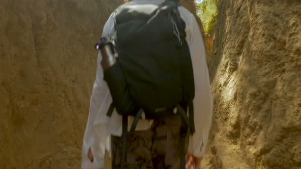Mann wandert mit Rucksack auf abgenutztem Bergweg mit hohen Wänden — Stockvideo