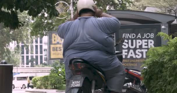 Мужчина с избыточным весом сидит на мотоцикле, ожидая мусульманских женщин, проходящих мимо — стоковое видео