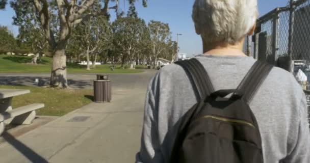Beau vieillard marchant le long d'un parc au bord de l'océan à côté d'une marina — Video