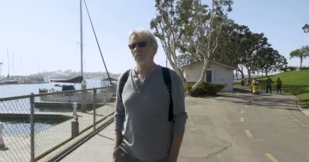 Hombre mayor caminando a lo largo de un sendero de playa junto a botes vacíos — Vídeos de Stock