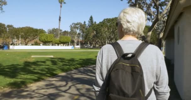 Gelukkig gezond senior man lopen door een park met een kleine rugzak — Stockvideo