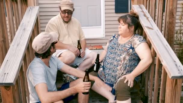 Três amigos sentados nos degraus do alpendre aplaudindo com garrafas marrons — Vídeo de Stock