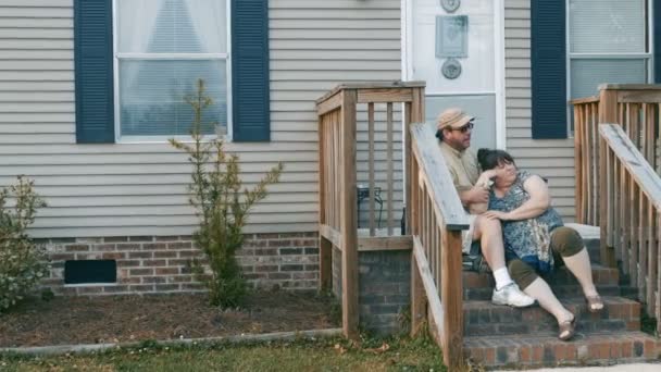 郊外住宅地における彼らのポーチで座ってプラス サイズ カップルの手順します。 — ストック動画