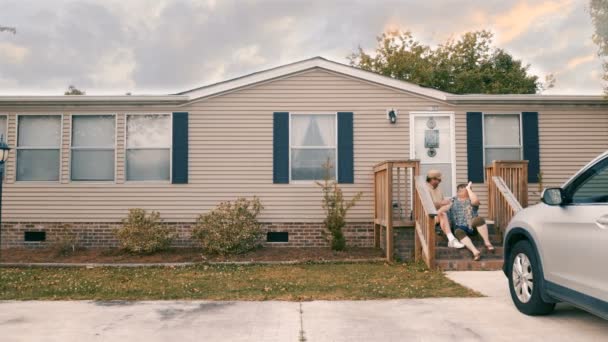 Мужчина и женщина сидят на ступеньках своего дома и дают друг другу пять — стоковое видео