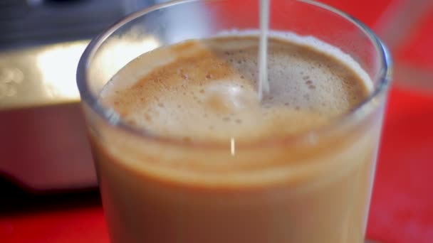 Leche espumosa vertida en la parte superior de un café con leche en una taza de vidrio transparente — Vídeos de Stock
