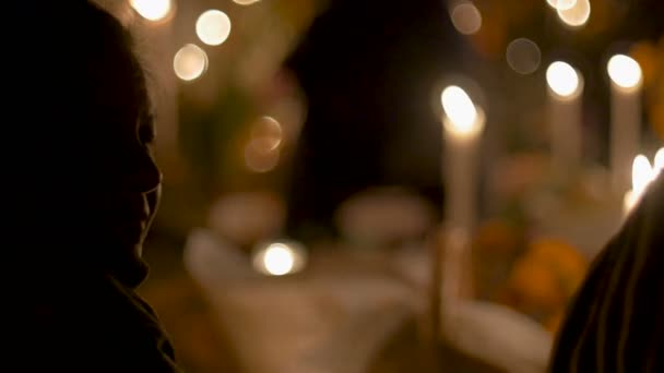 Пожилая женщина, покрытая шарфом, сидит при свечах в день смерти — стоковое видео