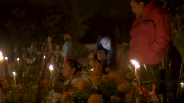 Young woman using cell phone at cemetery with her family at day of the dead — Stock Video