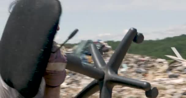 Человек выбрасывает мешок мусора и сломанное офисное кресло на свалку — стоковое видео